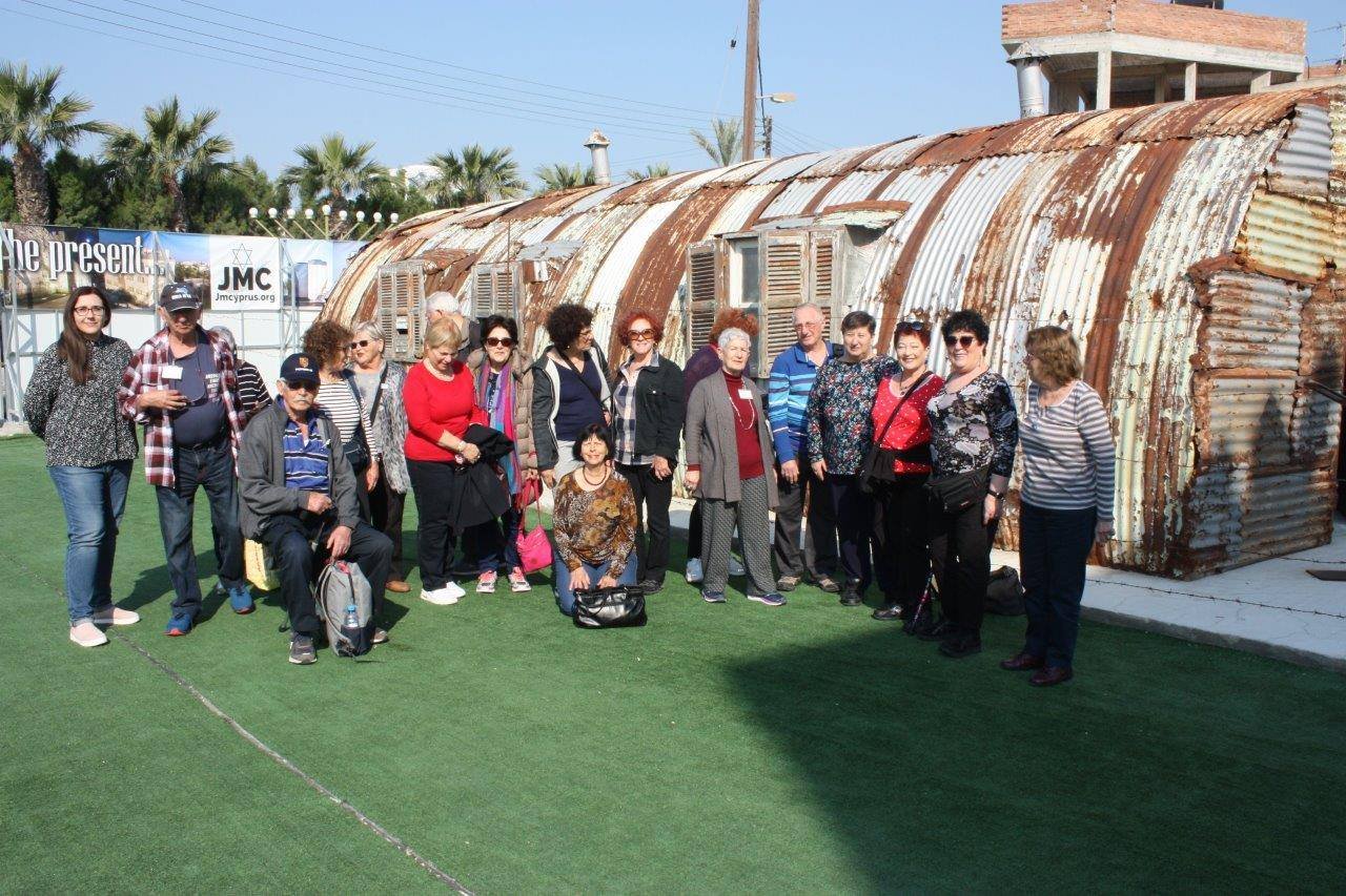 project manager skevi with a group of visitors who were born in camps, outside the nissen hut