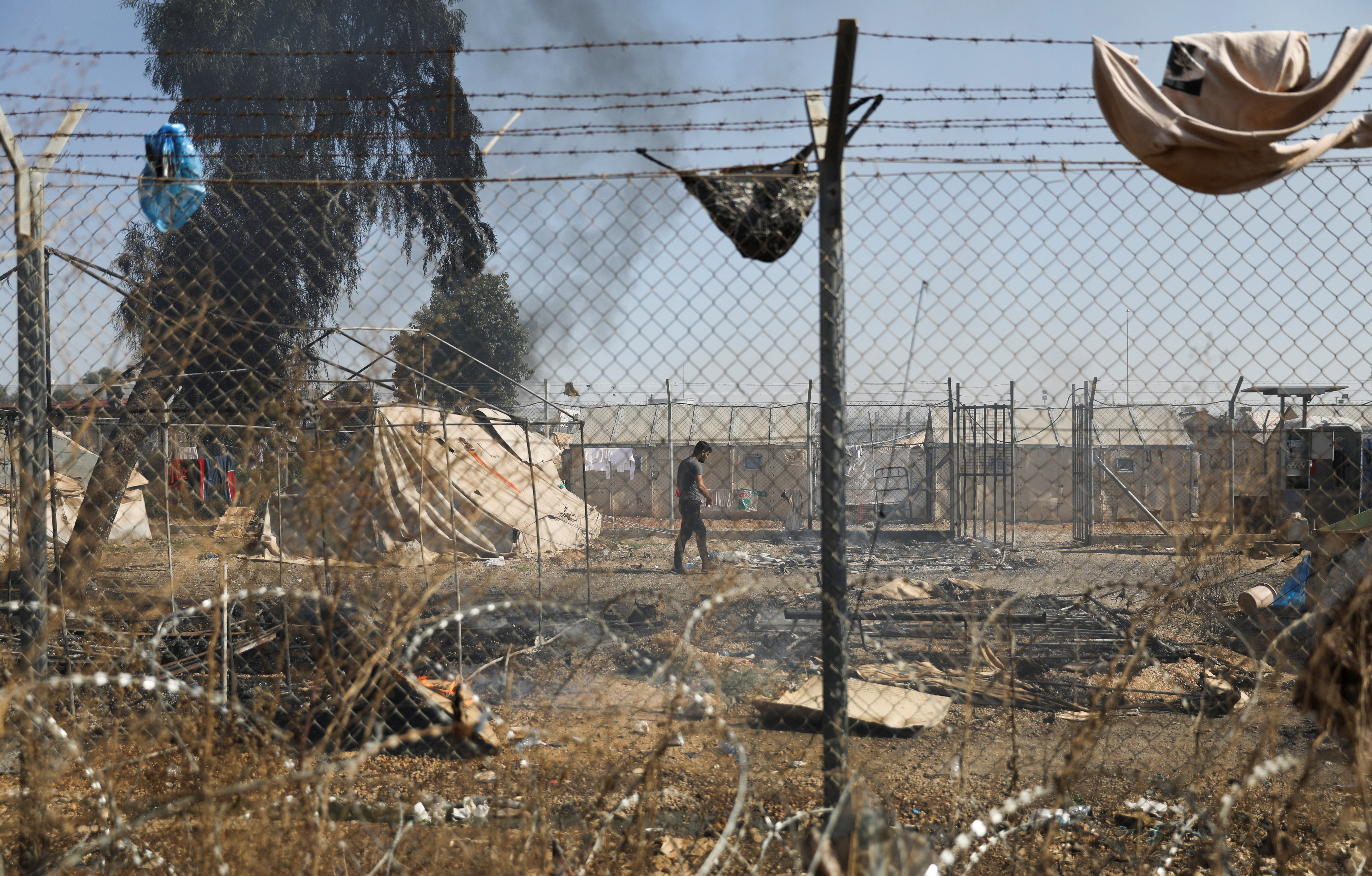 a migrant walks next to burned tents in pournara refugee camp during clashes on the outskirts of nicosia